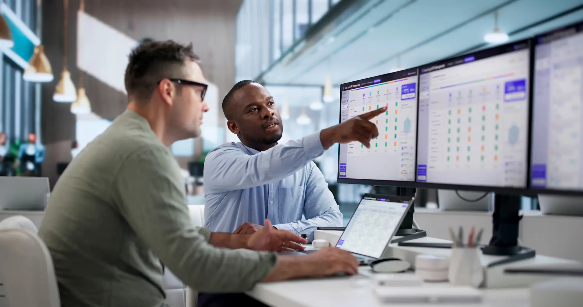 Two people at a desk reviewing a schedule on a large monitor